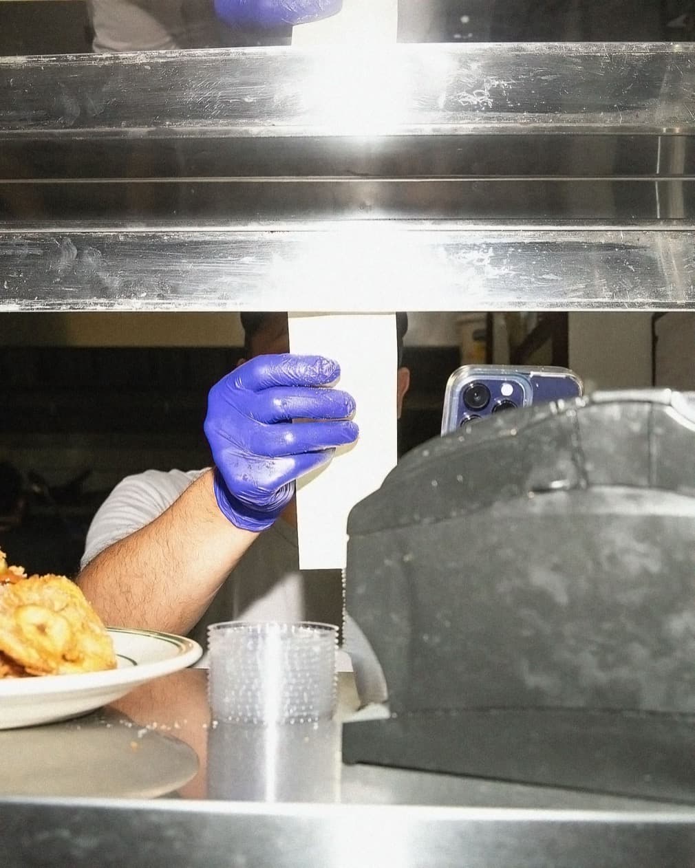 A gloved cook plating food on a busy line