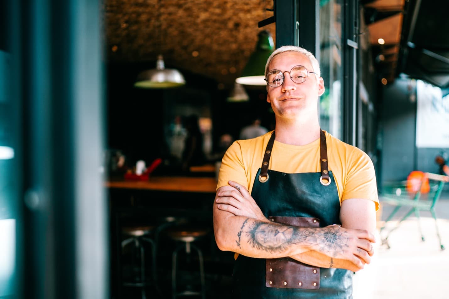 A chef in an apron standing in a dining room with arms crossed