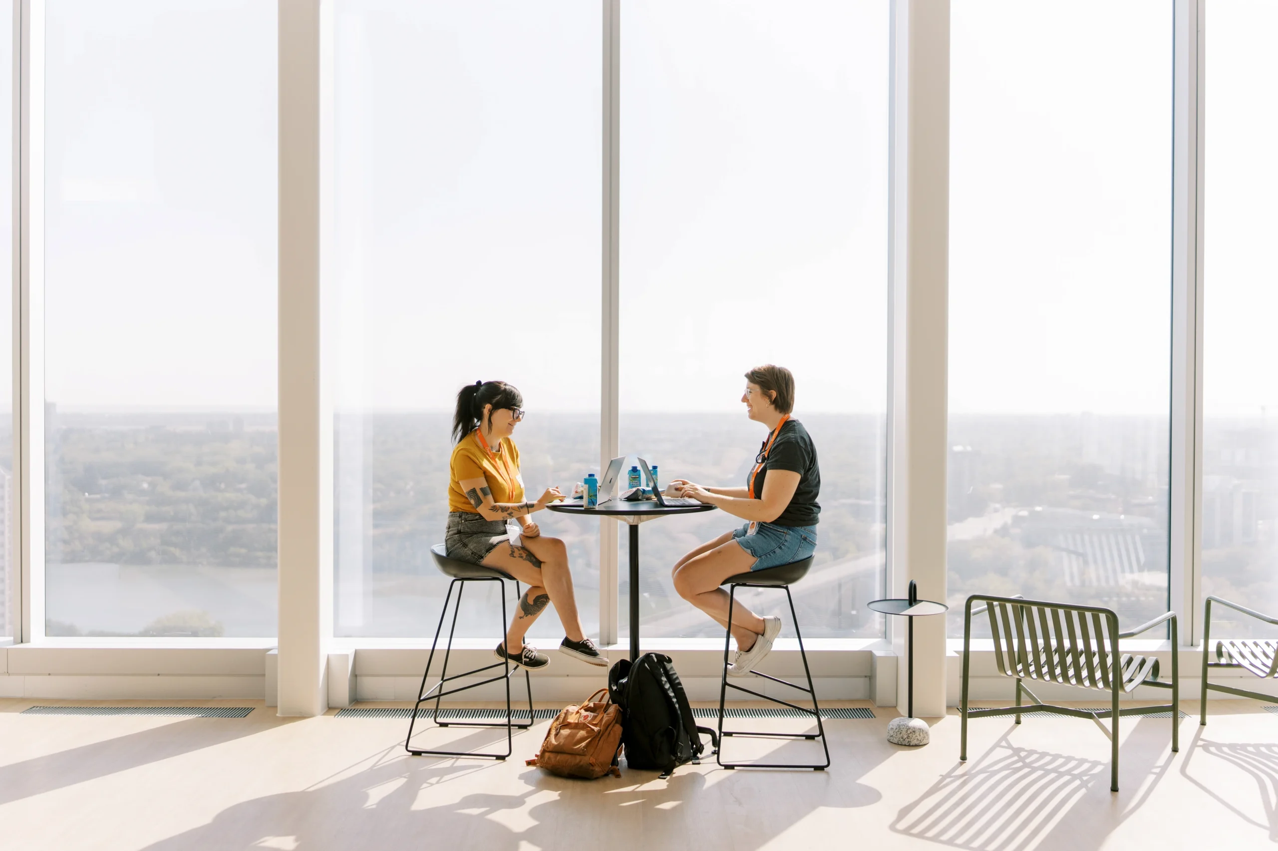 Two people discussing at table by large window.