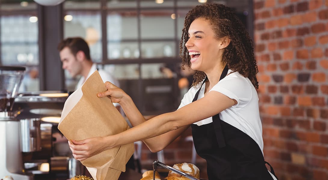 Smiling barista holding paper bag in cafe.