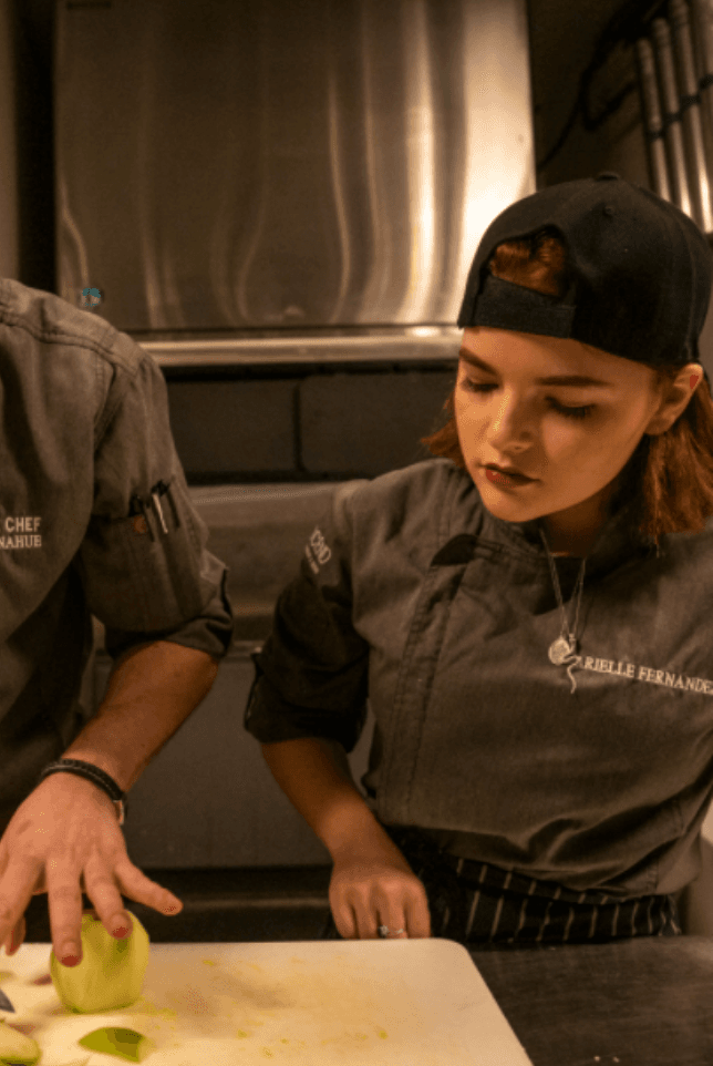 Woman sous chef wearing hat, watching someone chop apples off-camera