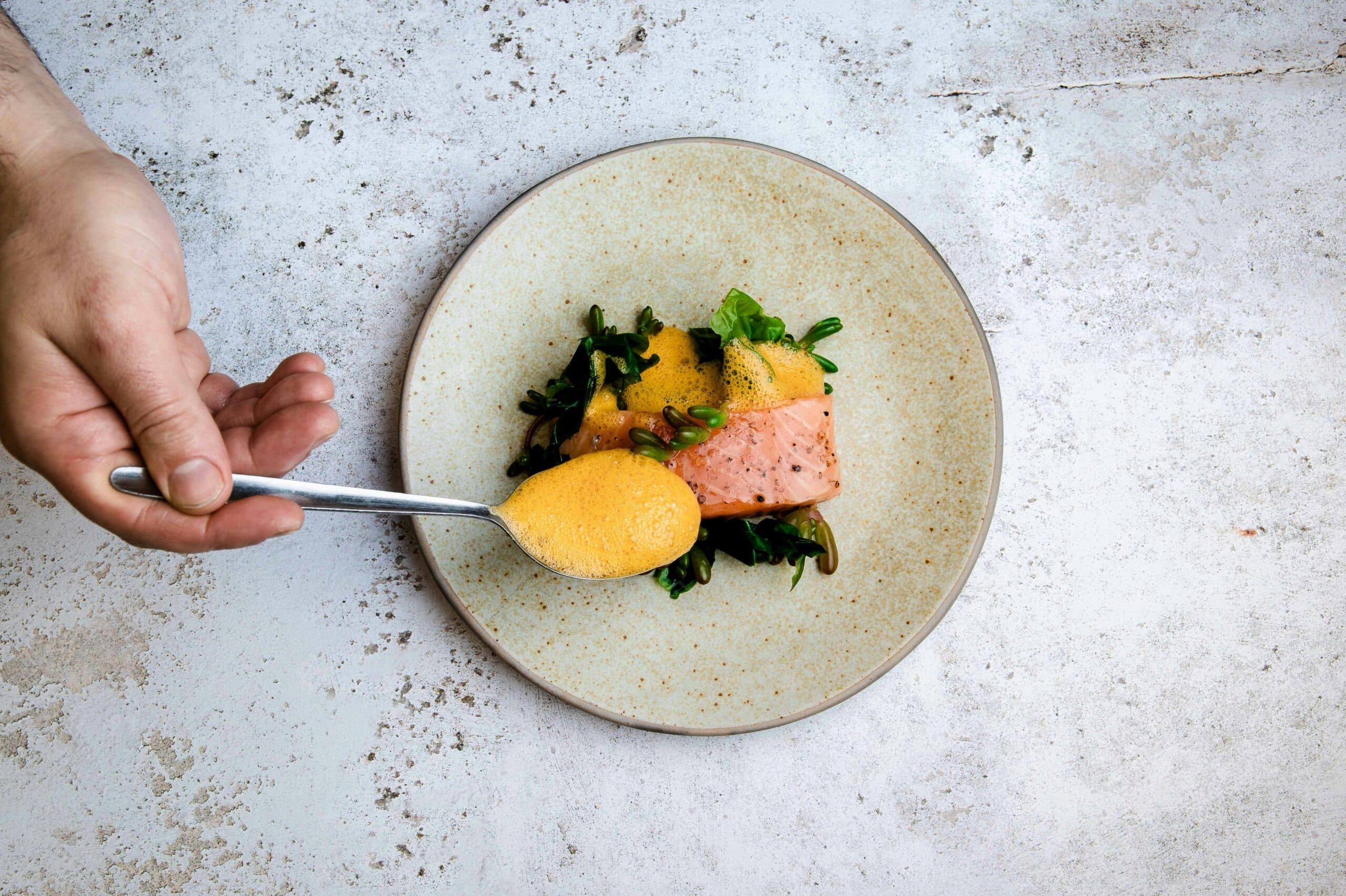 Plated restaurant dish of fish with hand holding sauce above it