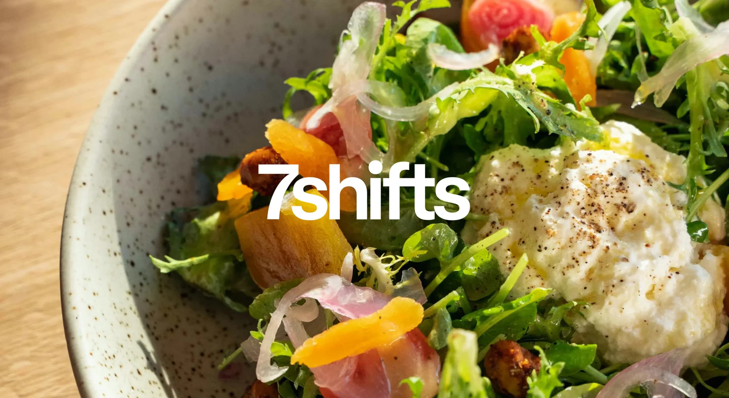 Bright bowl of salad being served at restaurant with white 7shifts logo overlay