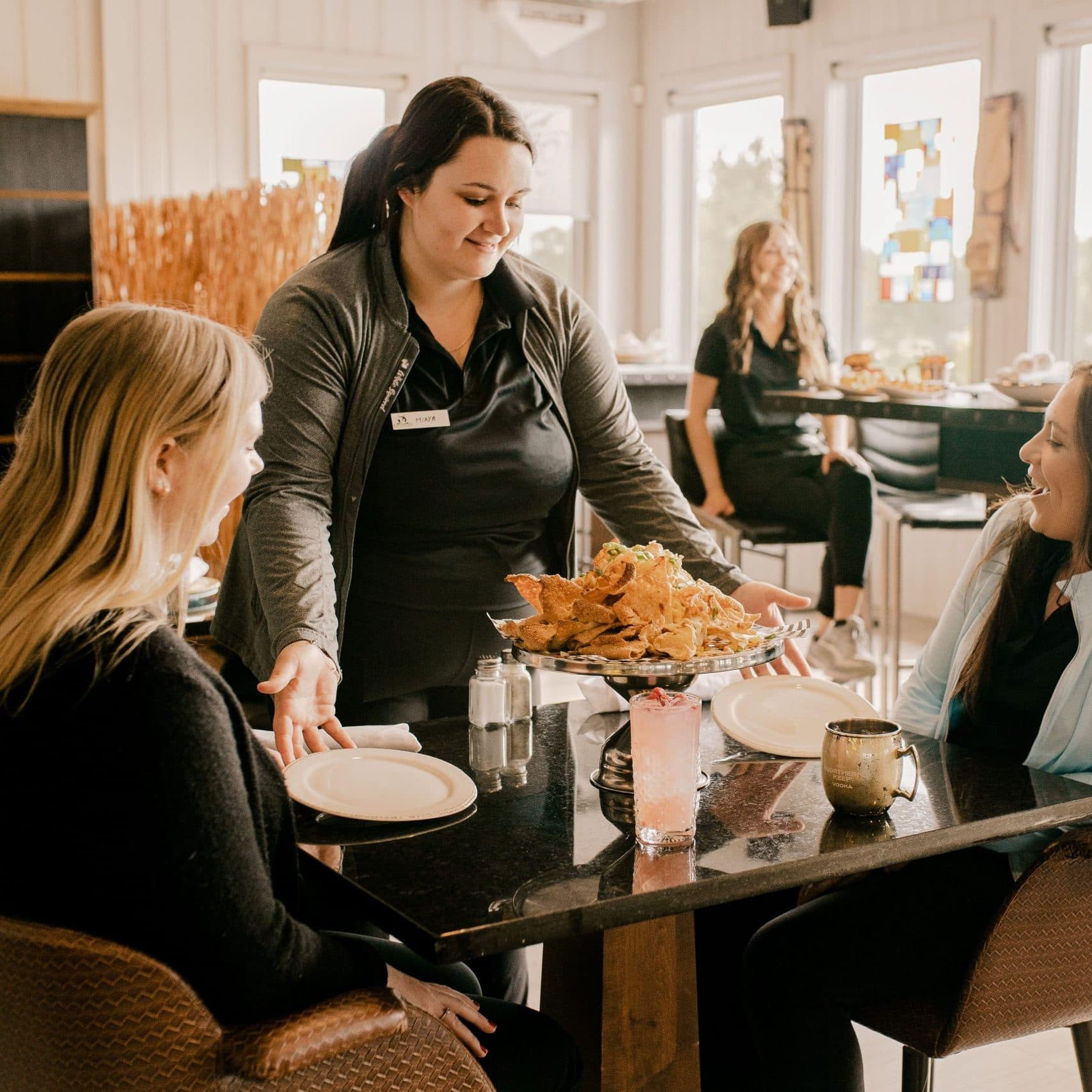 Female waitress at golf club serving two smiling women customers