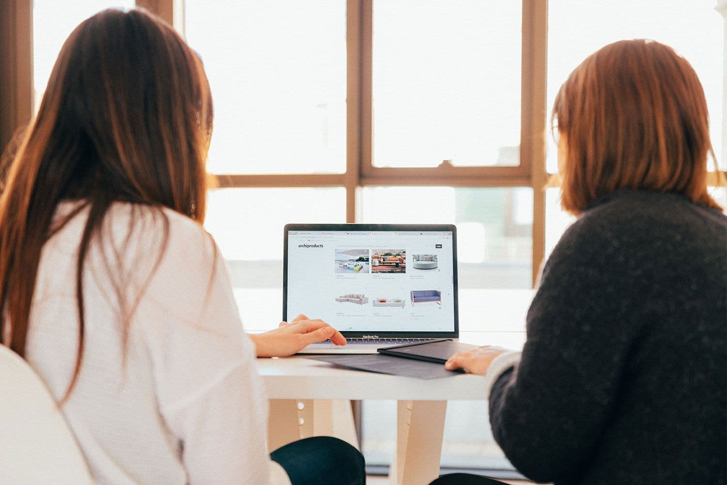 Two people browsing furniture website on laptop.