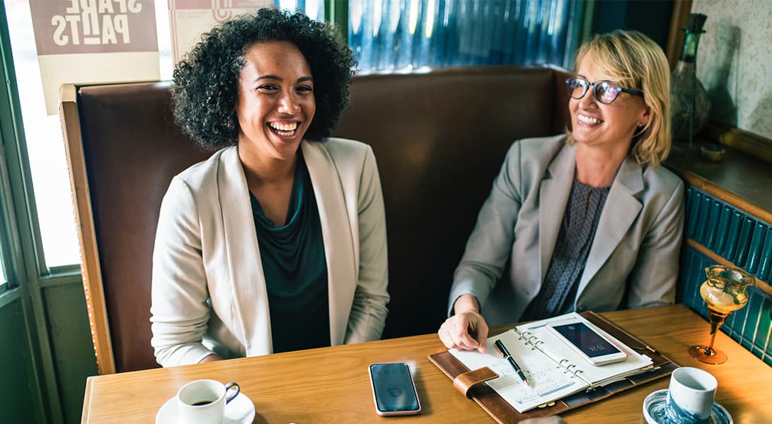 Two women smiling at a cafe table.