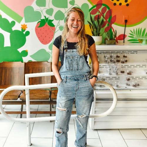 Smiling woman in denim overalls by colorful mural.