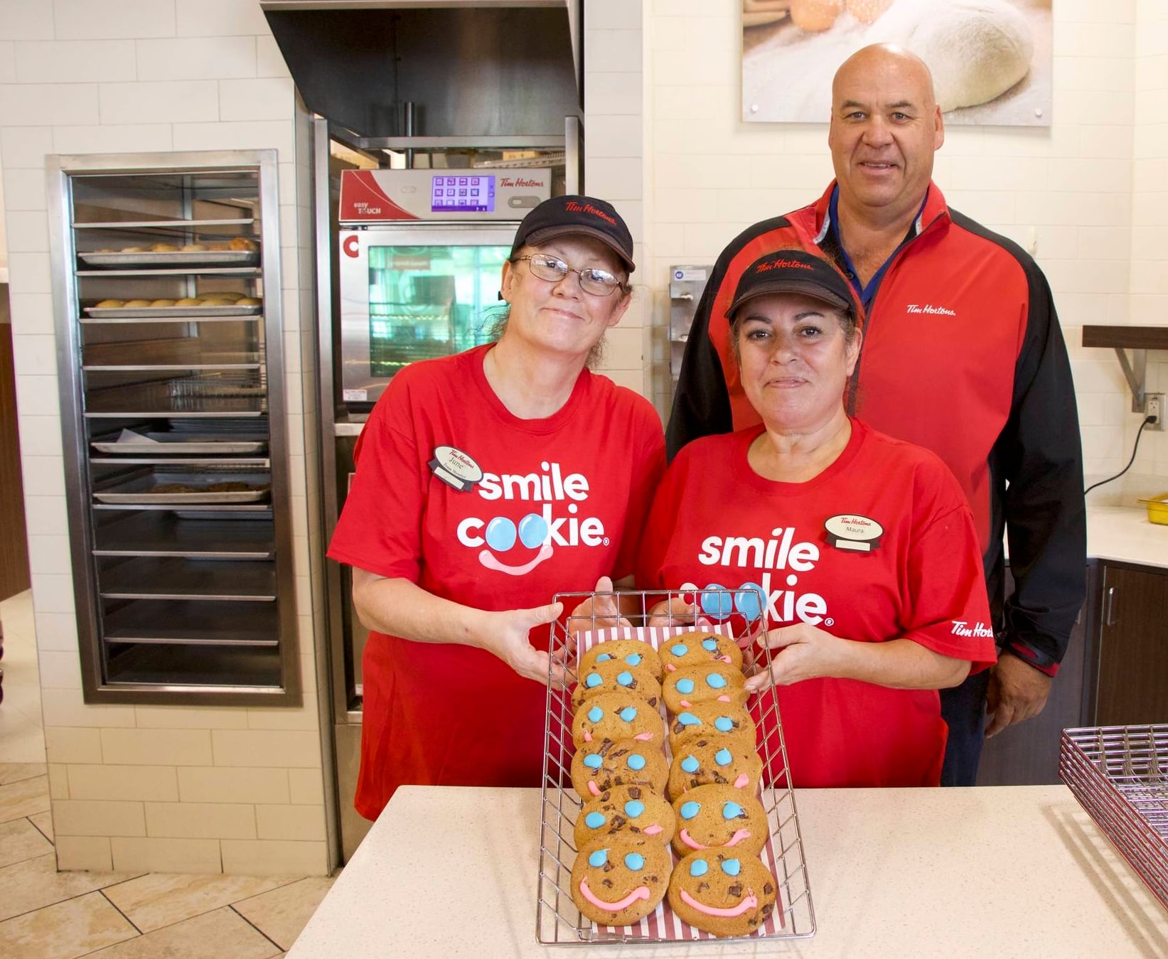 Employees presenting tray of smiling cookies.