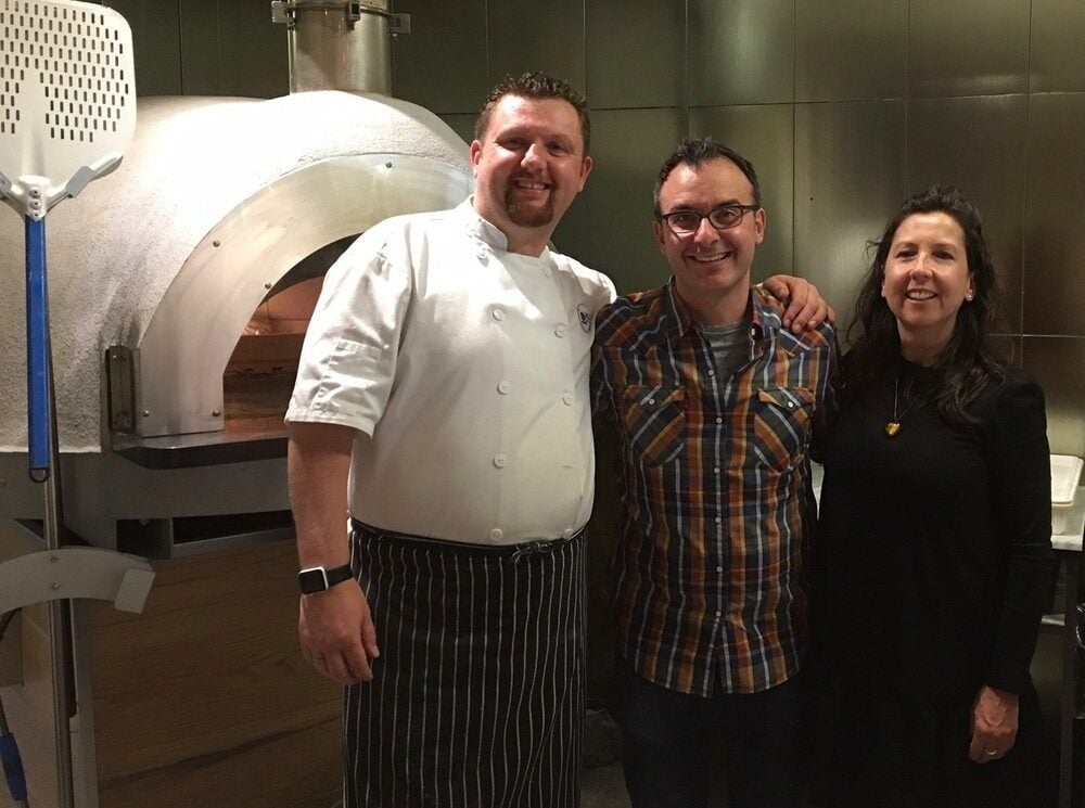 Chef and group posing by pizza oven.