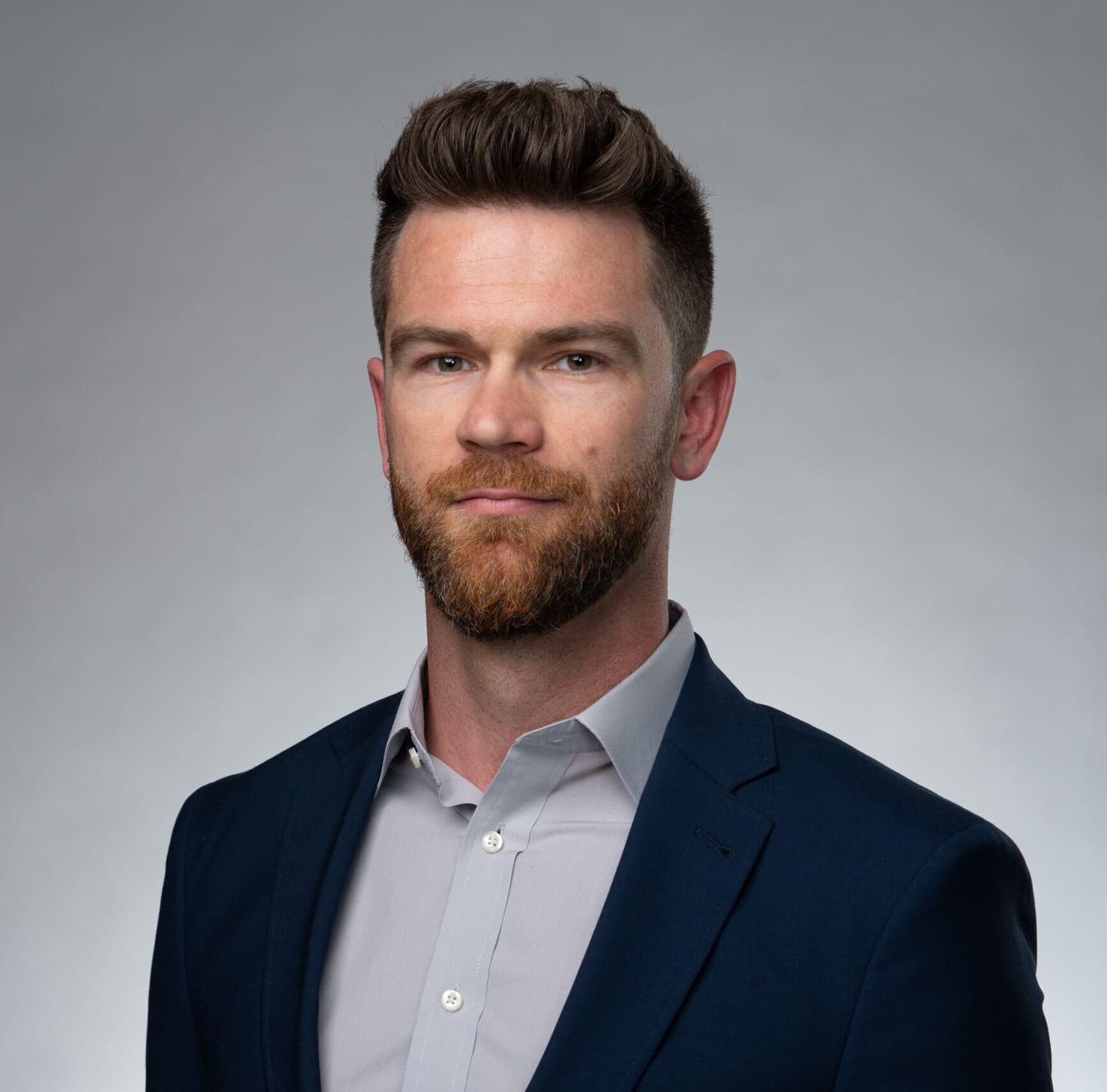 Man in suit with beard, neutral background.