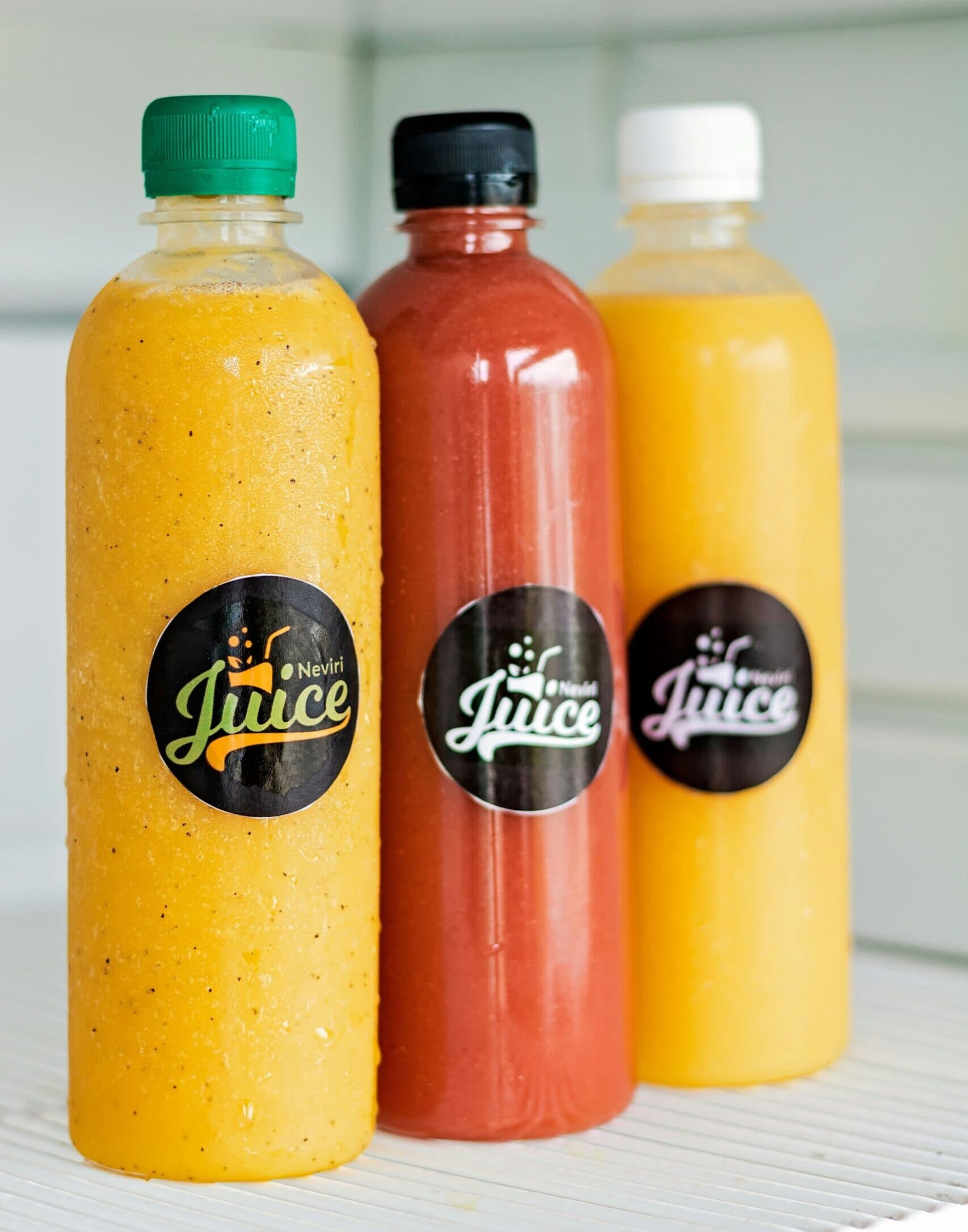 Three colorful juice bottles with labels on shelf.