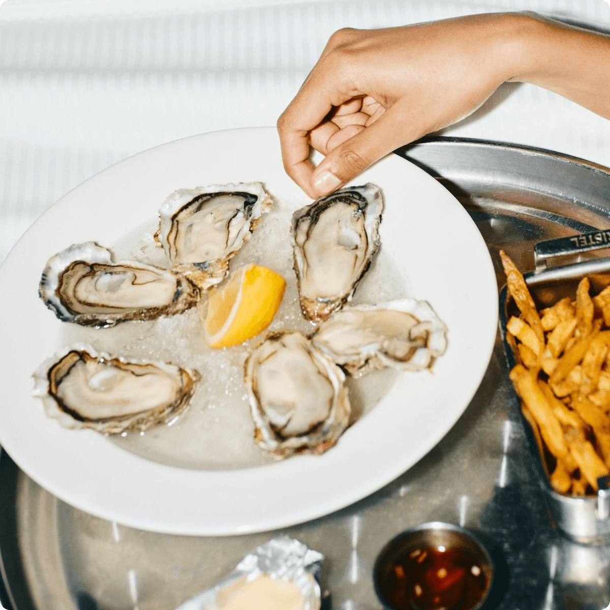 Hand reaching for oysters with fries and sauce.
