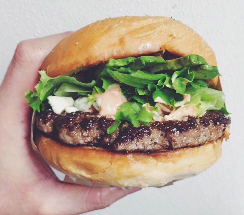 Hand holding a juicy hamburger with lettuce.