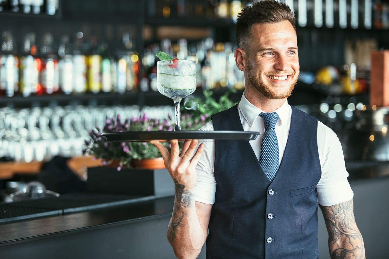 Smiling bartender serves cocktail in bar.