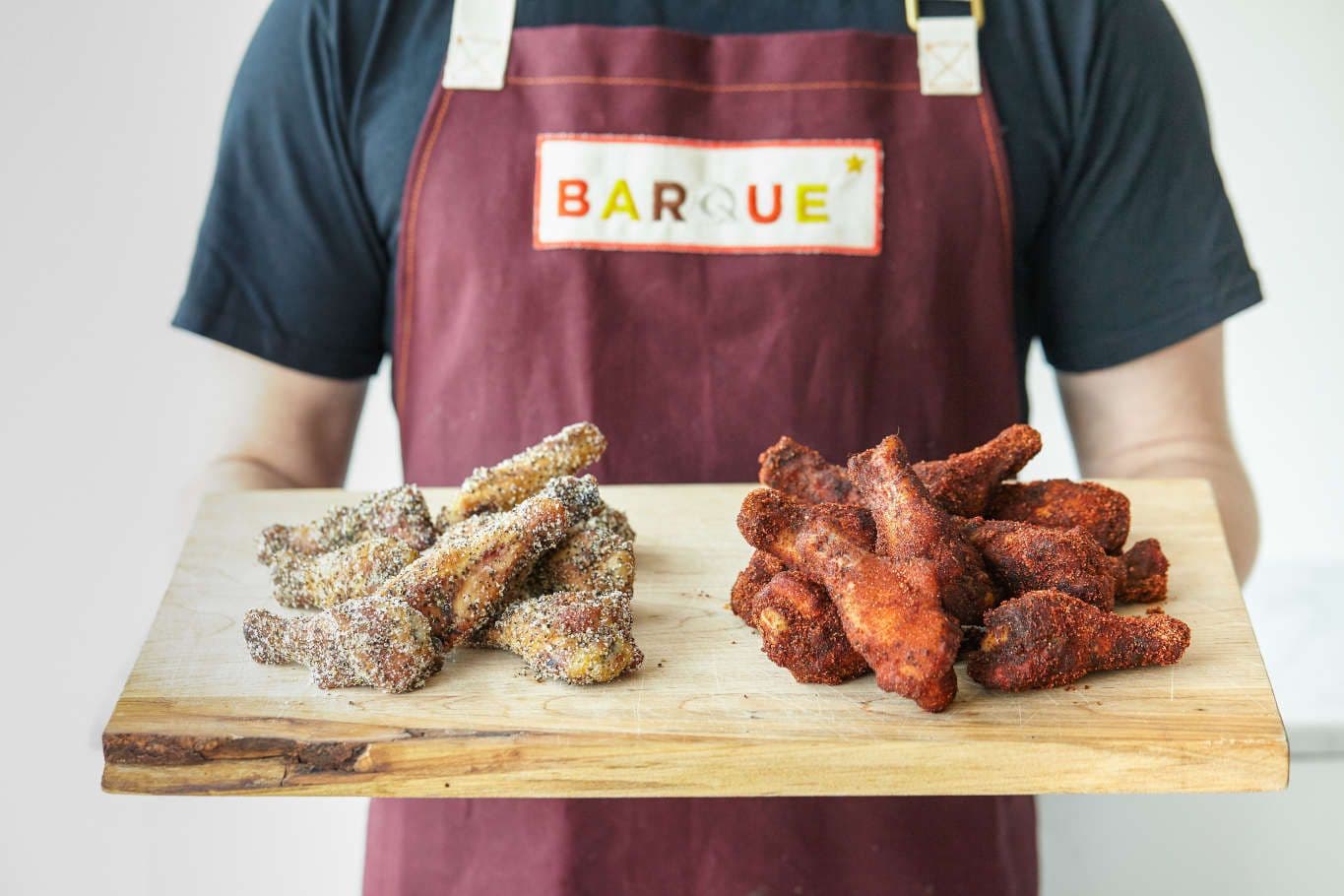 Two types of seasoned chicken wings on wooden board.