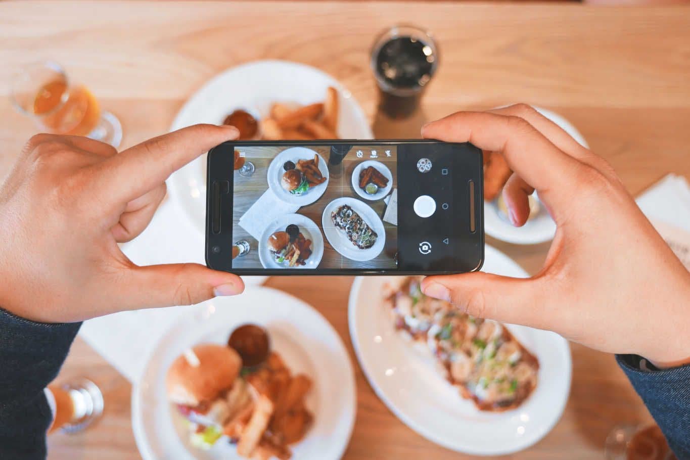 Hands photographing food on table with smartphone.