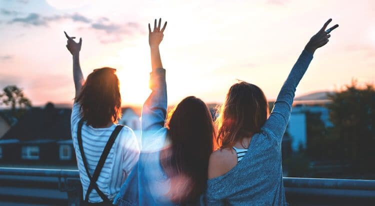 Three friends celebrating at sunset on a rooftop.