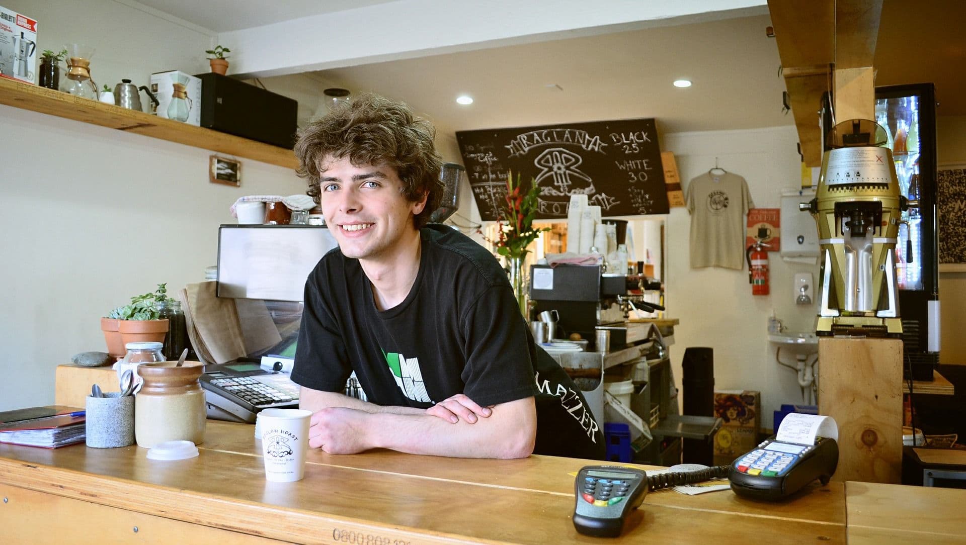 Barista smiling at coffee shop counter.
