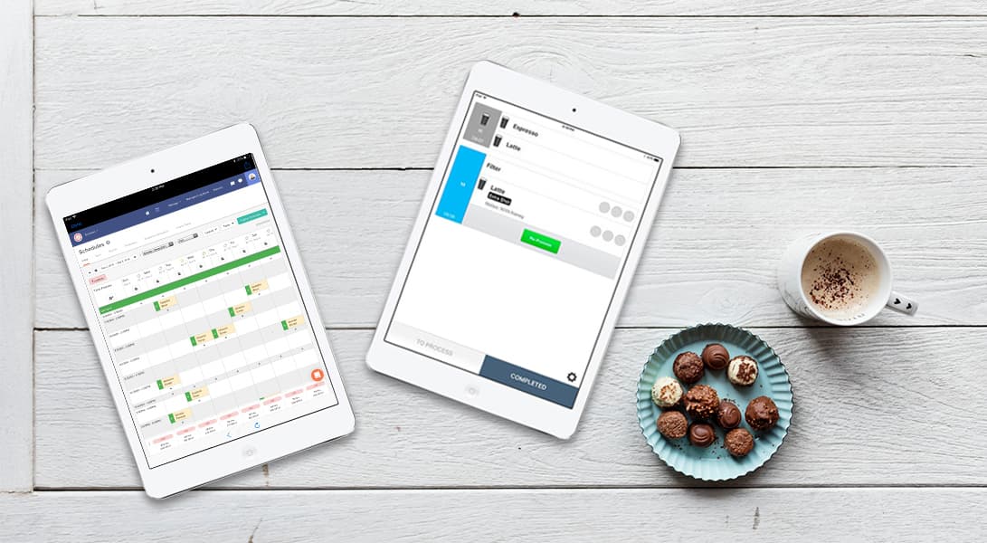 Two tablets with apps, coffee, and chocolates on table.