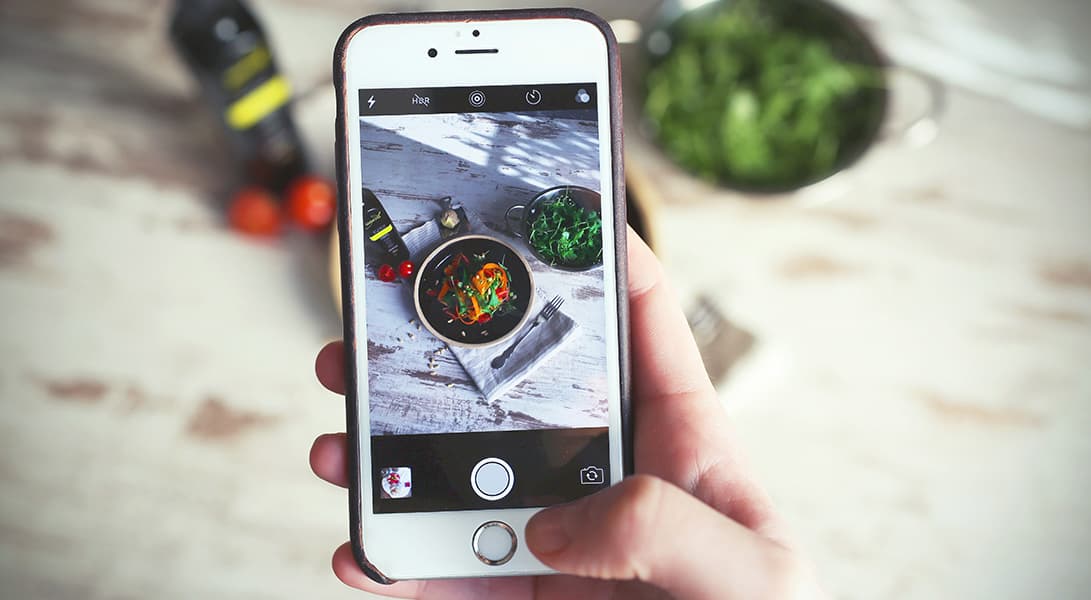 Smartphone photographing colorful vegetables on table.