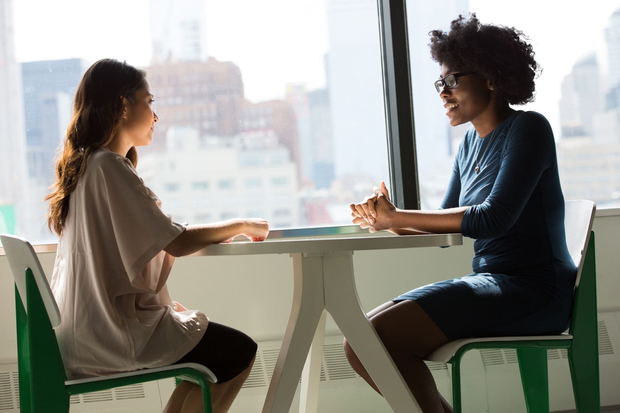 Two people conversing at a table by window.