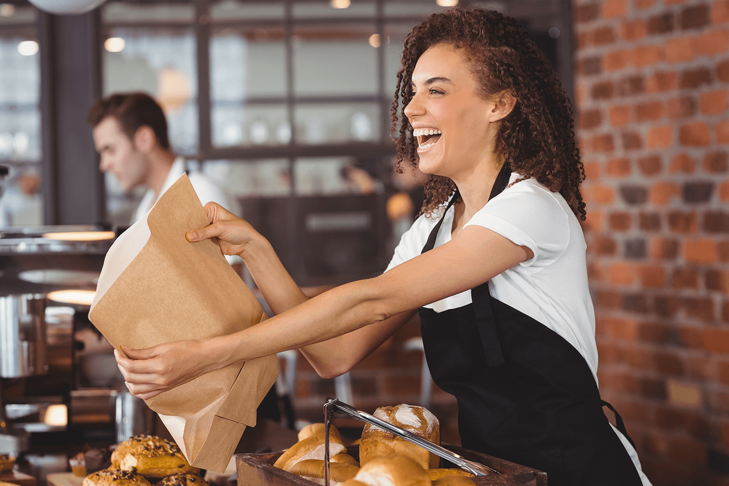 Smiling cashier packing pastry in paper bag