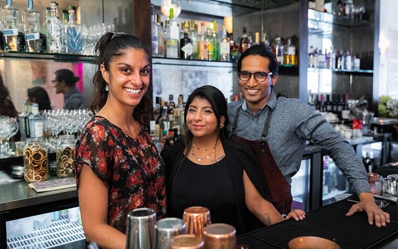 Smiling bar staff with drink selection behind counter.