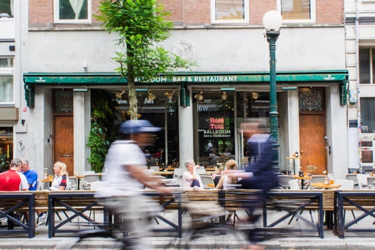 People passing lively restaurant with outdoor seating.