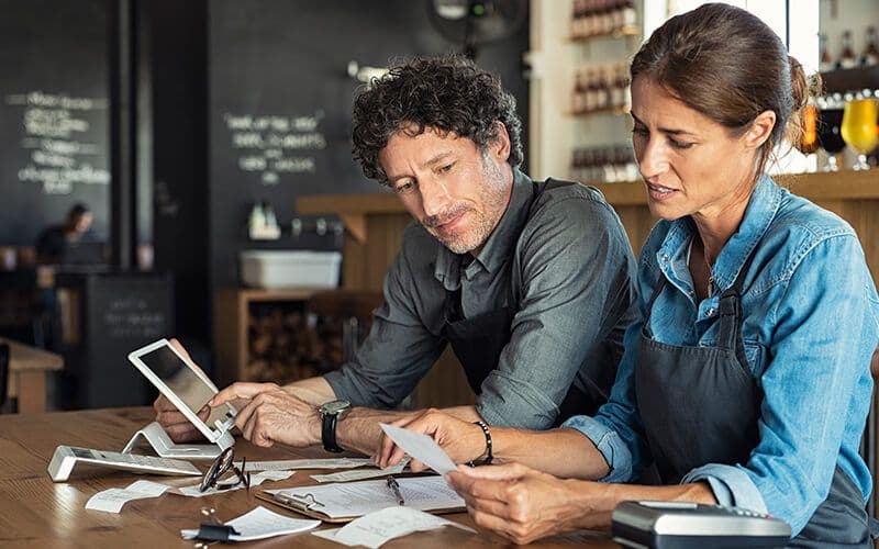 Two cafe owners reviewing documents at table.