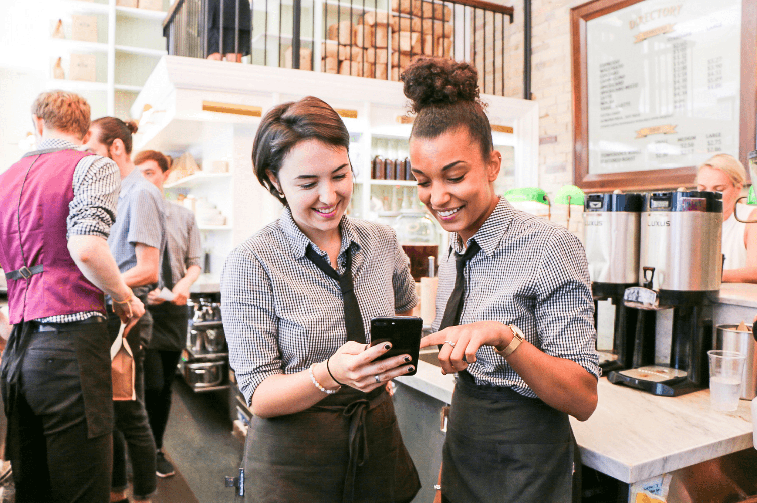 Baristas smiling and looking at a smartphone.