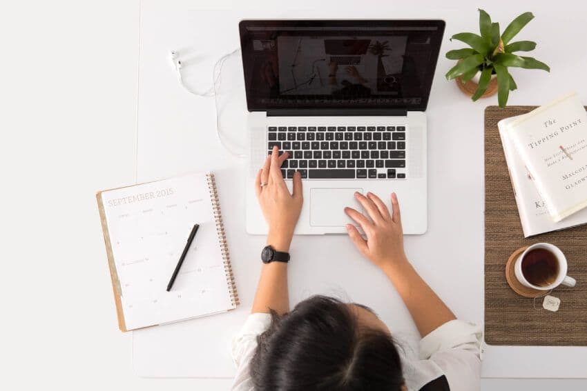 Person working on laptop with calendar and coffee.