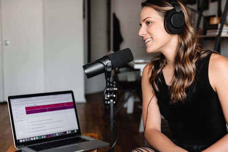 Woman recording podcast with microphone and laptop.