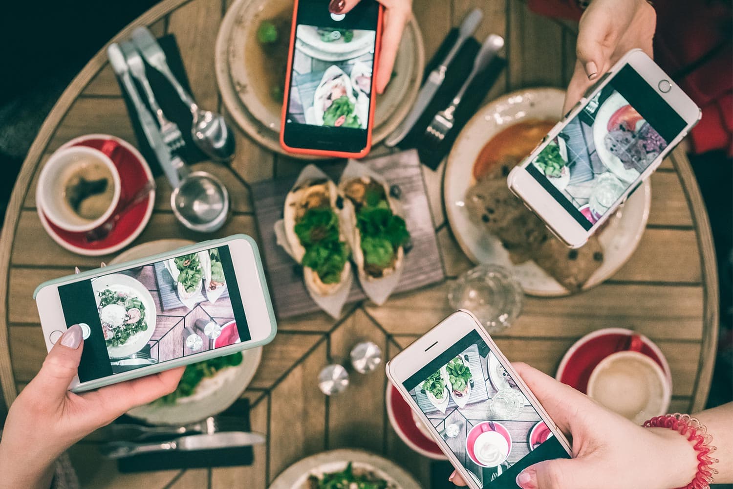 People photographing food with smartphones at restaurant table.