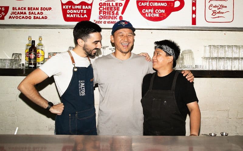 Three chefs smiling behind a restaurant counter.