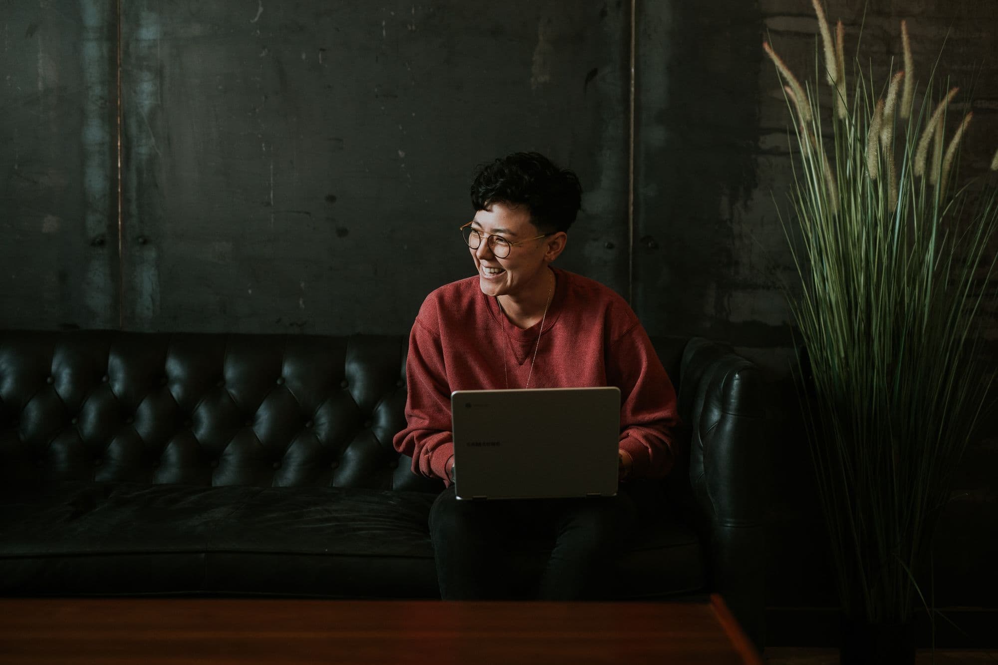 Person smiling with laptop on black couch