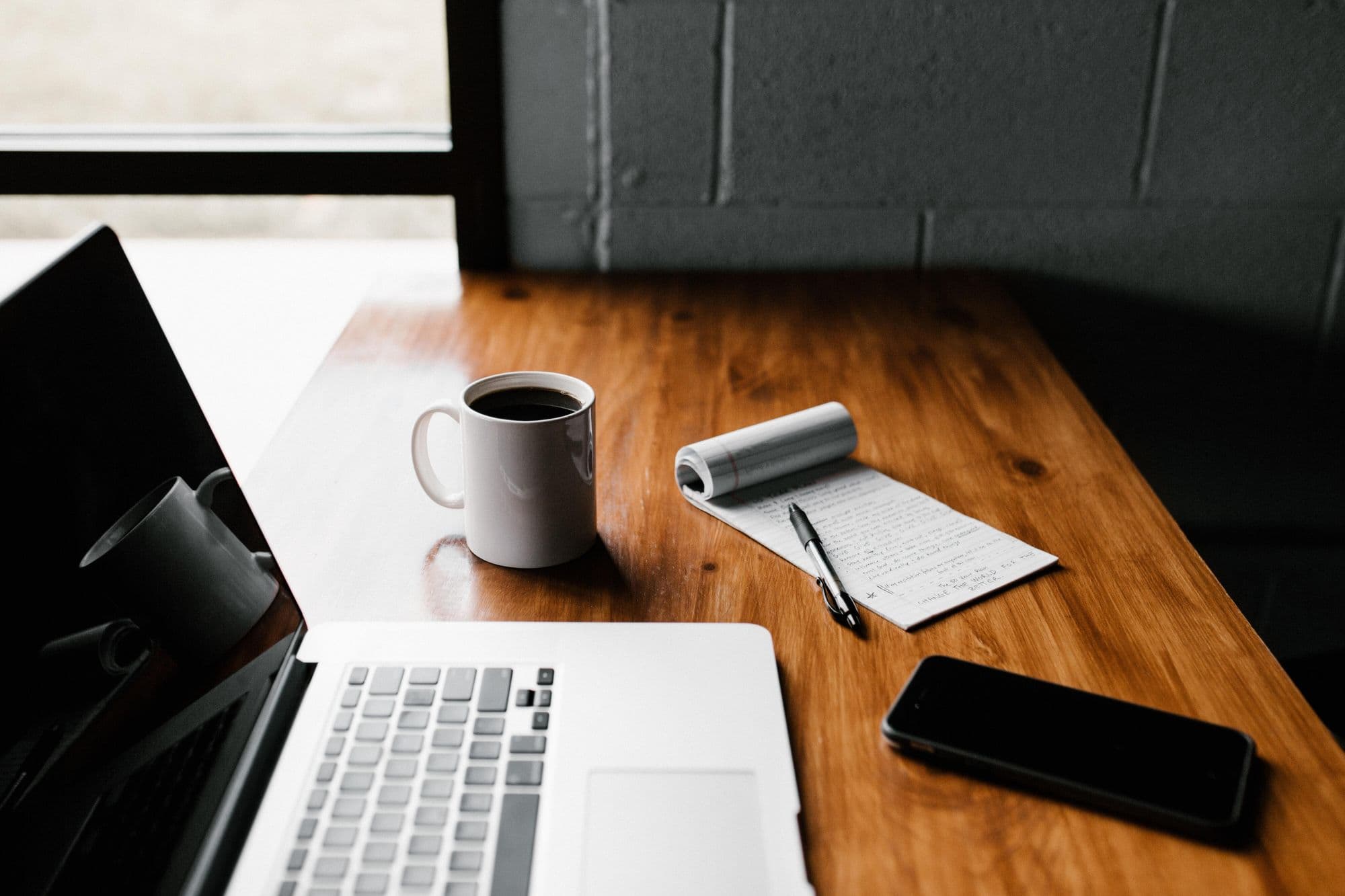 Workspace with laptop, coffee mug, notepad, and phone.