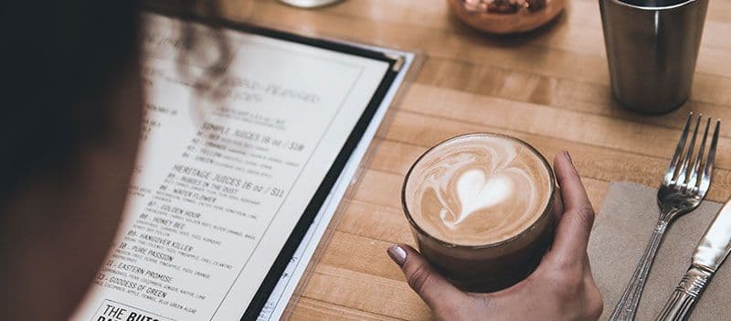 Person holding latte near menu on table.