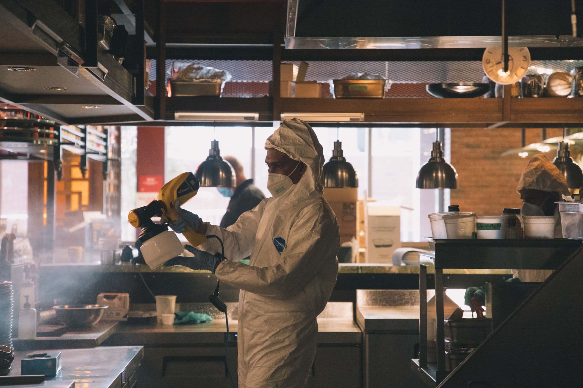 Worker disinfecting restaurant kitchen with spray equipment