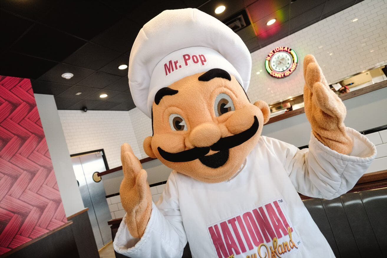 Mascot chef in restaurant with mustache and hat.