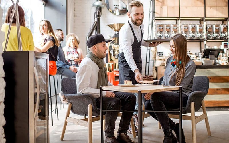 Barista serving cake to couple at cafe table.