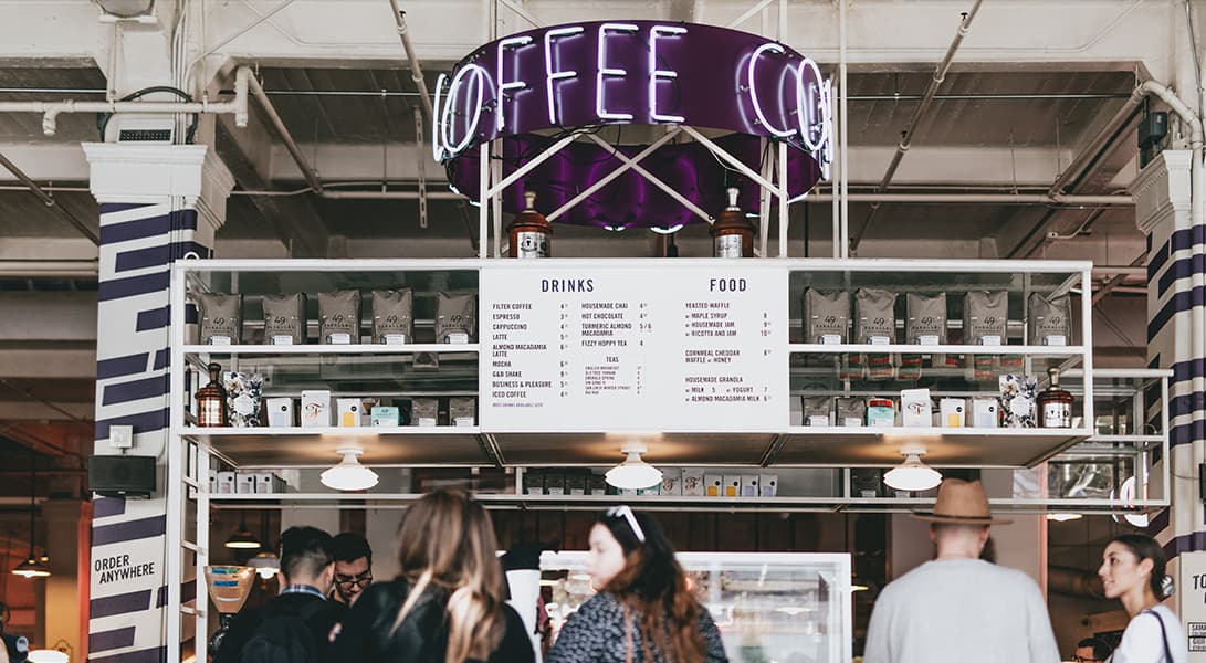 Busy coffee stand with menu and neon sign.