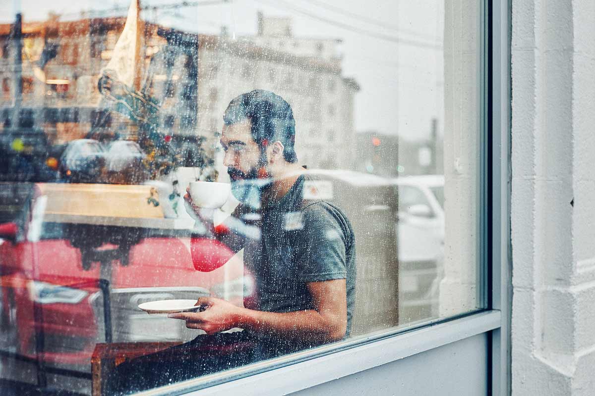 Man drinks coffee inside a rainy café.