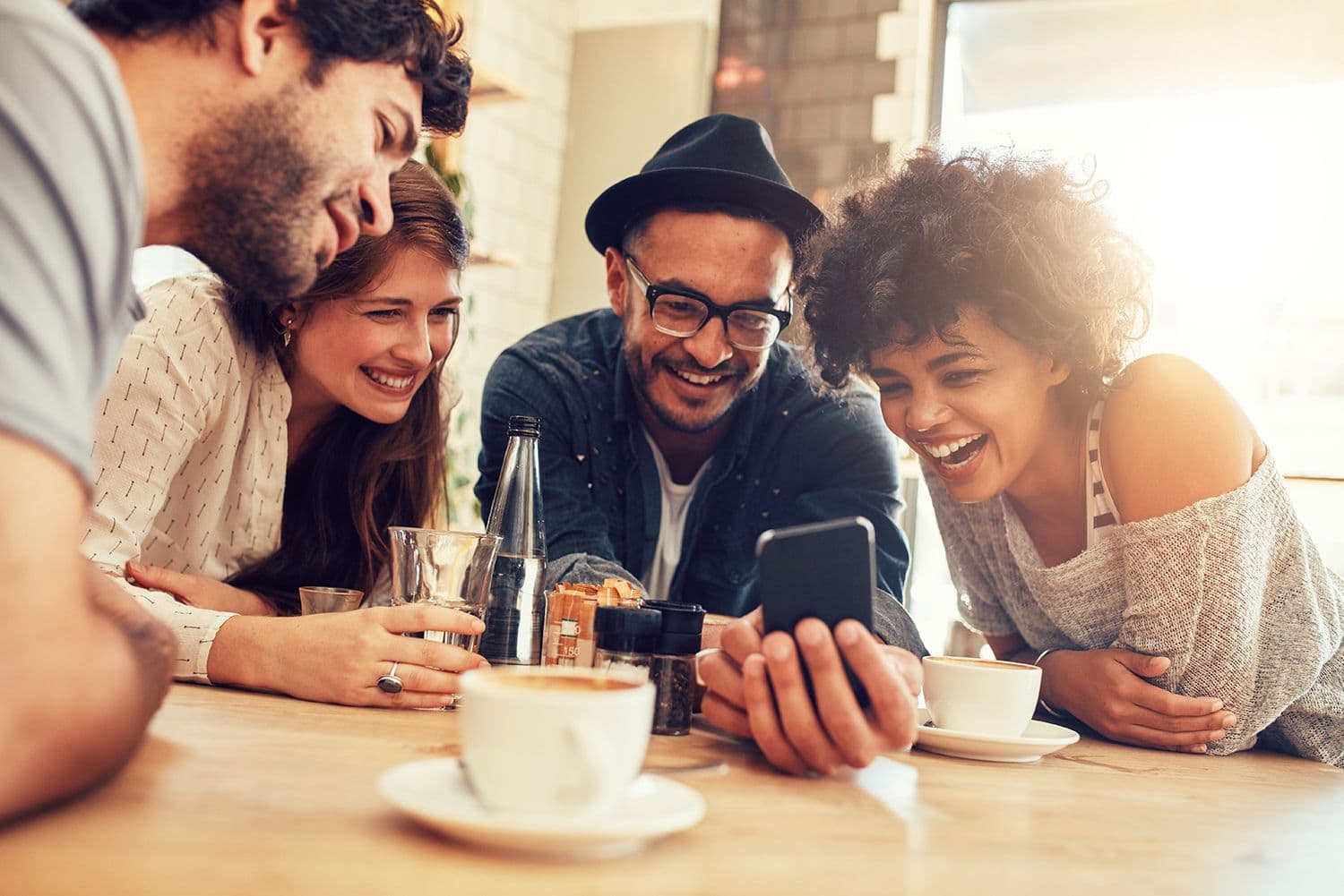 Friends laughing at phone in cafe.