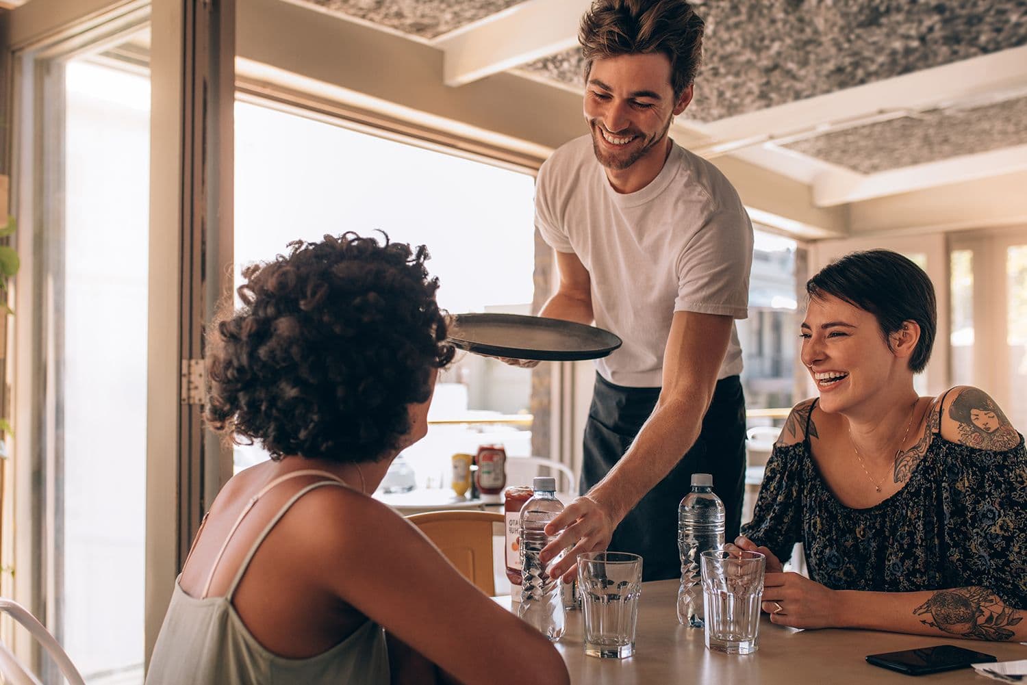 Smiling waiter serves drinks to seated diners.