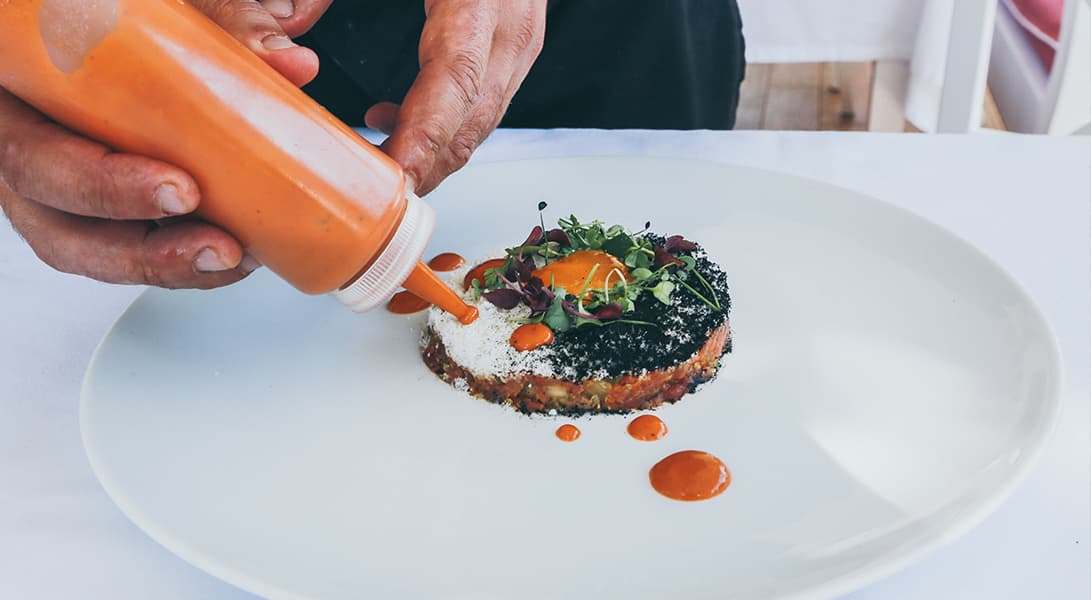 Chef garnishing dish with red sauce