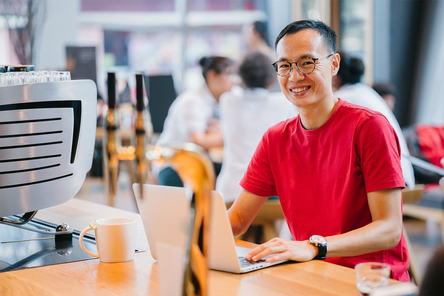 Smiling person in red shirt using laptop in cafe.