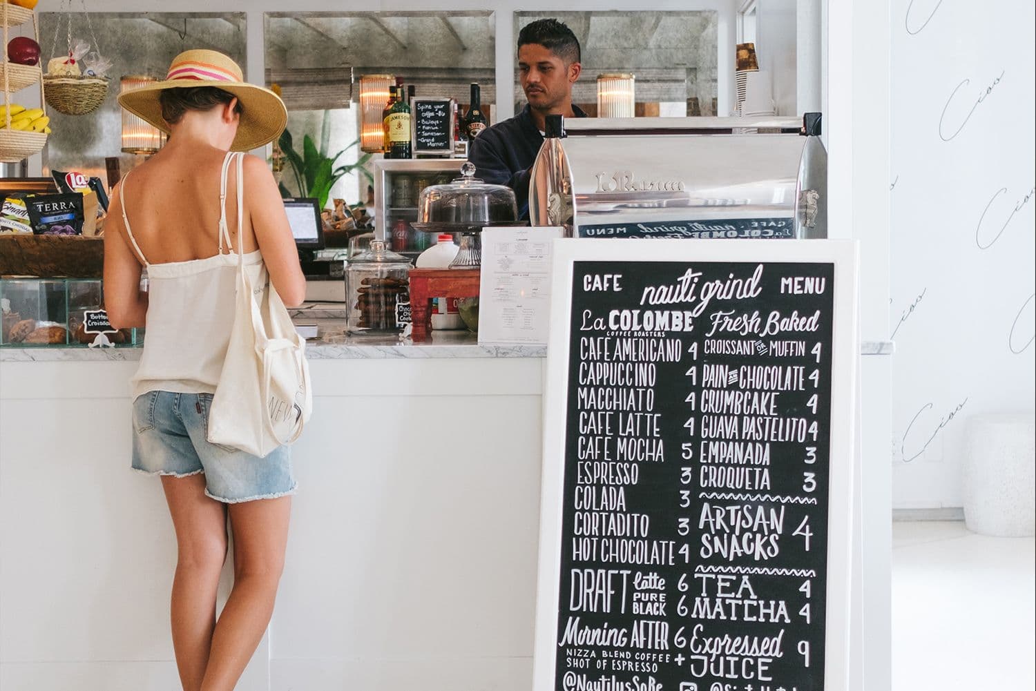 Customer ordering at café counter with menu board.