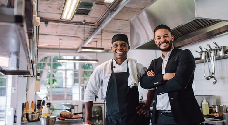 Chef and manager smiling in restaurant kitchen.