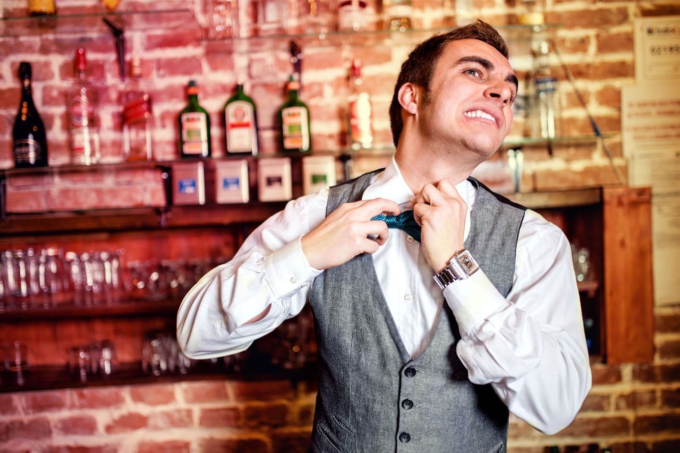 Man adjusting bow tie in bar setting.