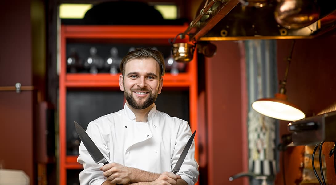 Chef smiling with crossed knives in kitchen